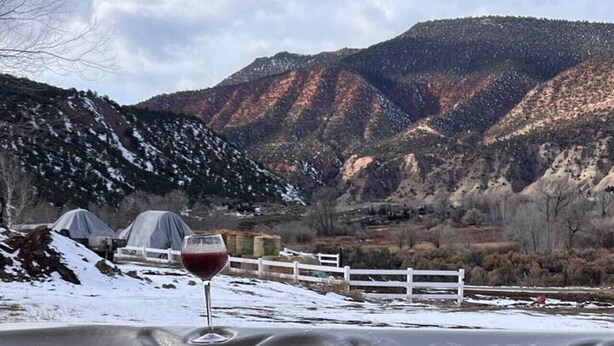 Un bain  à remous, un verre de vin rouge à la main, entouré d’un paysage enneigé et avec des montagnes en toile de fond.