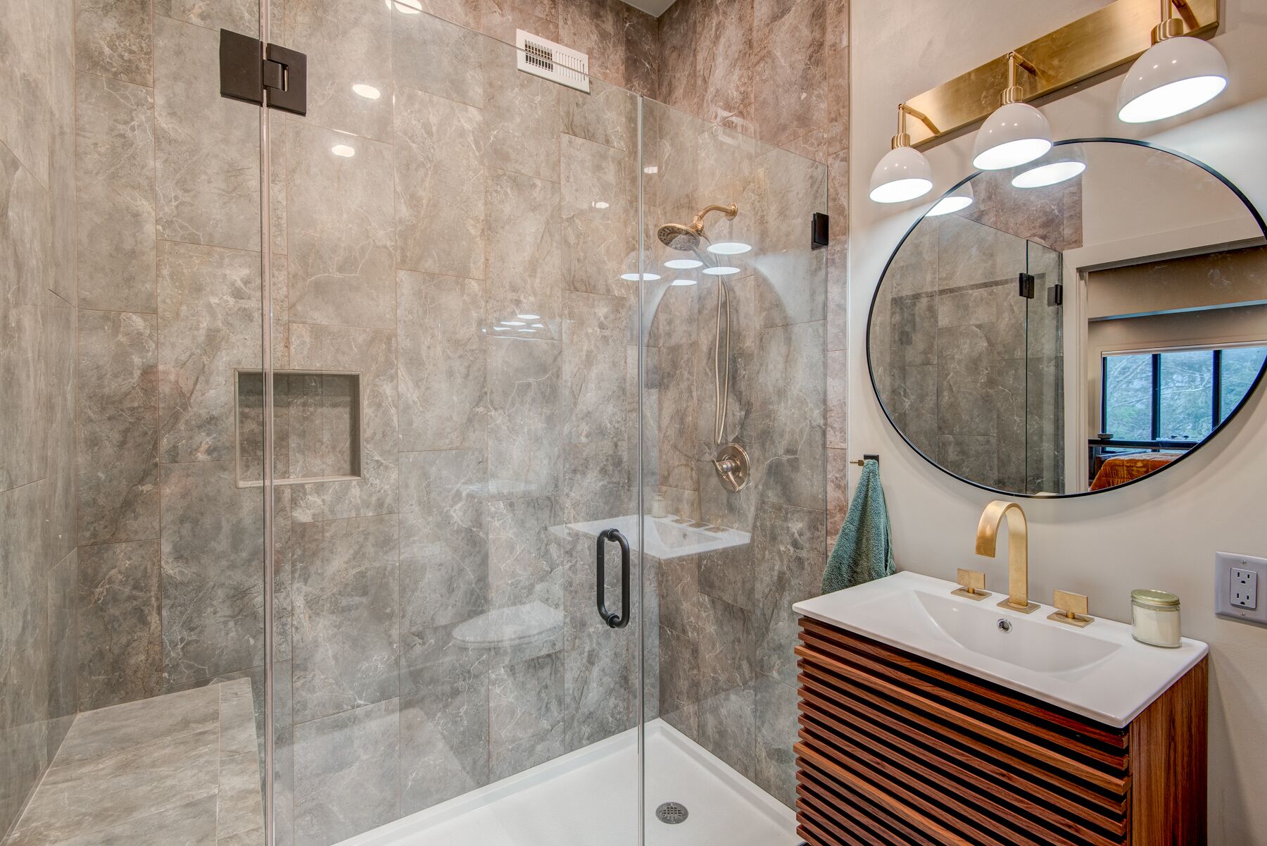 A modern bathroom with a glass-enclosed shower, a round mirror, and a wooden vanity.