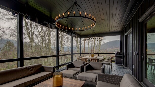 Un espace extérieur abrité, aménagé avec une table, des chaises et une grande fenêtre donnant sur le paysage environnant.