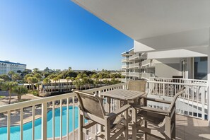 Un balcón con piscina, mobiliario exterior y vistas a palmeras y otros edificios.