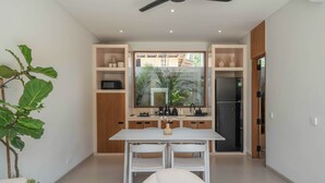 A modern kitchen with white cabinetry, a dining table, and chairs. There is a large window with a view of a residential area. - Dreamscape Haven  (Canggu)