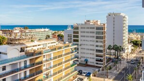 Ein mehrstöckiges Hotel mit Balkonen, Blick auf das Meer und einem Parkplatz.