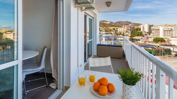 Ein Balkon mit Tisch, zwei Stühlen, einem Blumentopf und Blick auf die Stadtlandschaft.