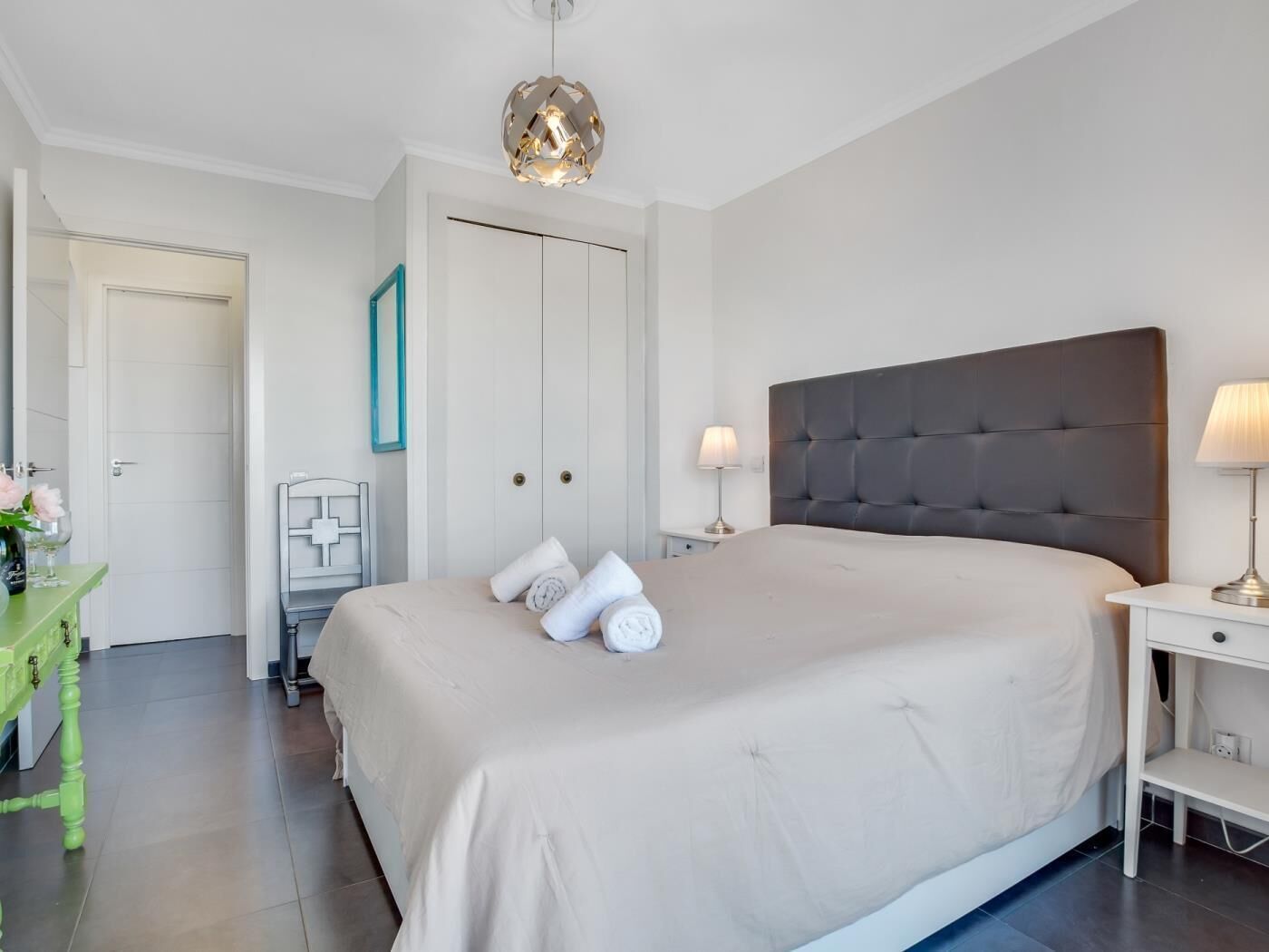 Un dormitorio ordenado con una cama grande, una mesita de noche con lámpara, un aparador y un armario.