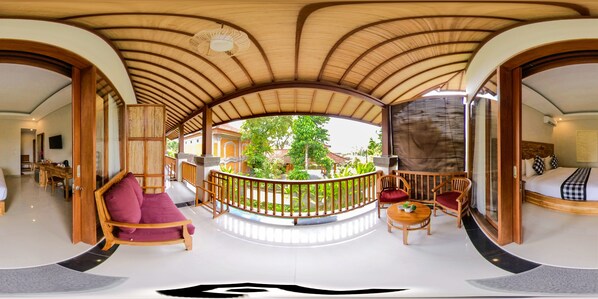 A spacious room with a curved ceiling, a balcony with a wooden railing, a round wooden table, and a bed with a checkered bedspread.