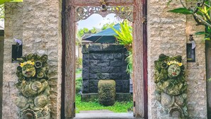 A stone entrance with a decorative archway, a small step leading up to it, and two lion statues on either side. - Ari Cottages (Ubud)