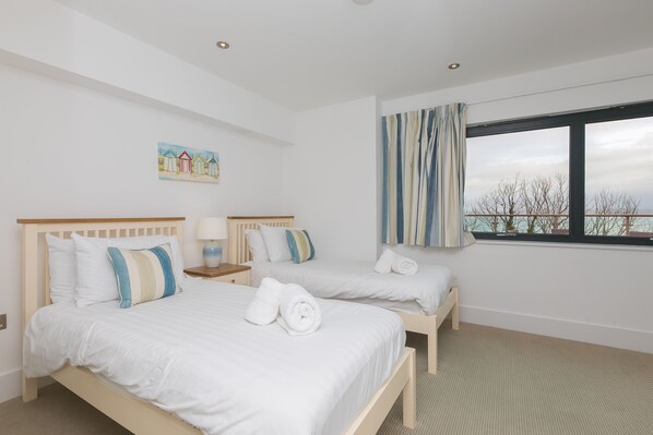 A hotel room with two beds, a large window with curtains, a painting on the wall, and a view of trees outside. - Number One Peninsula – Sleeps 4 – Sea Views – On-Site Parking – Dog Friendly - Outside Space (St Ives)