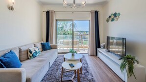A living room with a sofa, a small table, a TV, and a balcony with a view.