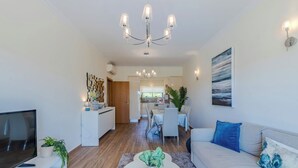 A modern living room with a TV, sofa, coffee table, and a dining area with chairs and a table.
