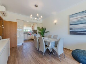 Una cocina moderna con armarios blancos, un área de comedor con una mesa de mármol y un cuadro abstracto grande en la pared.