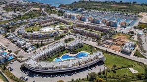 An aerial view of a coastal resort with a central swimming pool, multiple buildings, and a marina.