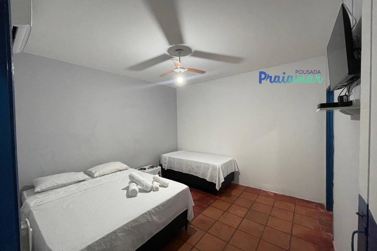 A small, clean room with two single beds, a ceiling fan, and a TV mounted on the wall.