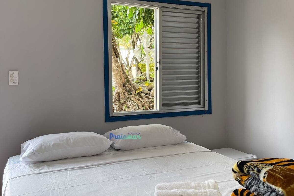 A hotel room with a bed, white pillows, a window with a view of greenery, and a tiger plush toy.