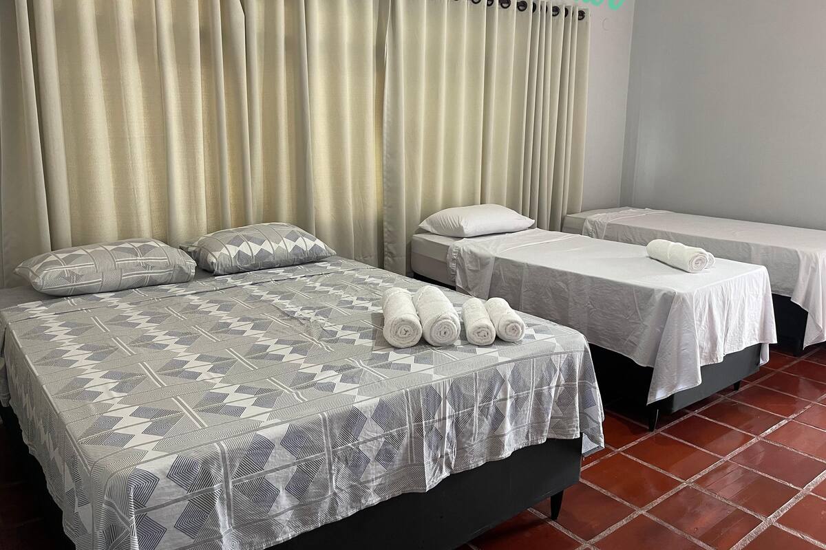 A hotel room with two beds, each with a white bedspread and pillows. There are towels neatly rolled on the beds.
