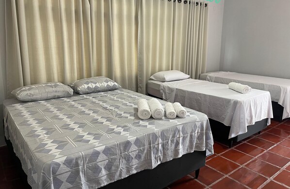 Une chambre d’hôtel avec deux lits, chacun recouvert d’une courtepointe blanche et agrémenté d’oreillers. Des serviettes sont soigneusement pliées et posées sur les lits.