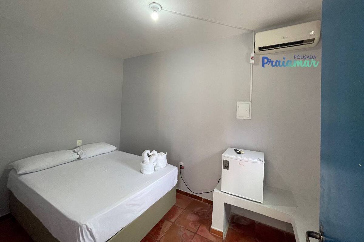 A hotel room with a bed, a small table with a heater, and an air conditioning unit on the wall.