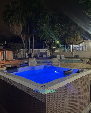 Un bain à remous avec un éclairage bleu, entouré de meubles de jardin et de palmiers.