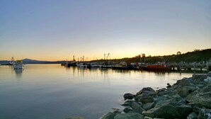 Un port tranquil amb vaixells amarrats, un litoral rocosos i una muntanya a la distància.
