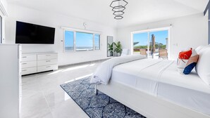 A modern bedroom with a large bed, a flat-screen TV, and a view of the outdoors.