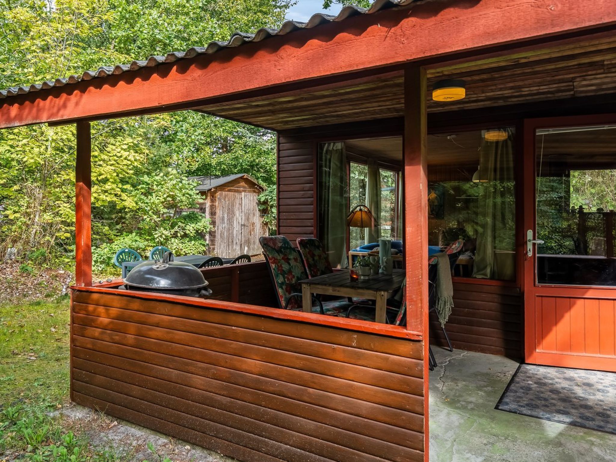 Una cabaña de madera con un porche cubierto, una parrilla y una mesa de comedor con sillas.