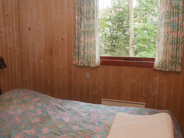 Een slaapkamer met houten wanden, een bed met een kleurrijke sprei en een raam met bloemen gordijnen.