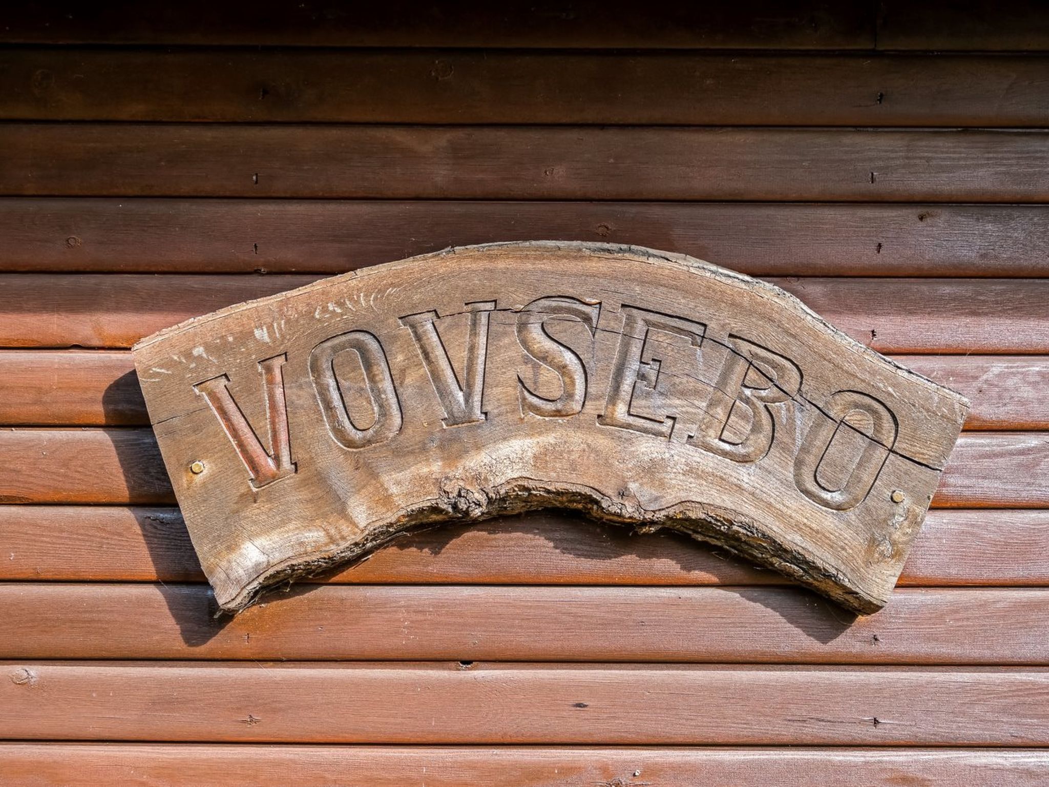 Un cartello di legno con l'iscrizione 'VOVSEBO' fissato a una parete di legno.