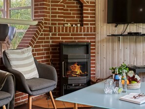 A cozy room with a brick fireplace, a comfortable chair, a table with drinks and snacks, and a flat-screen TV mounted on the wall.