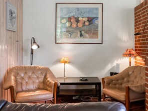 A room with two leather armchairs, a table, a lamp, and a framed painting on the wall.
