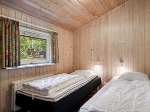 A room with wooden walls, a window with curtains, two beds, and a radiator.
