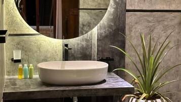 A bathroom with a round mirror, a white sink, and a potted plant.
