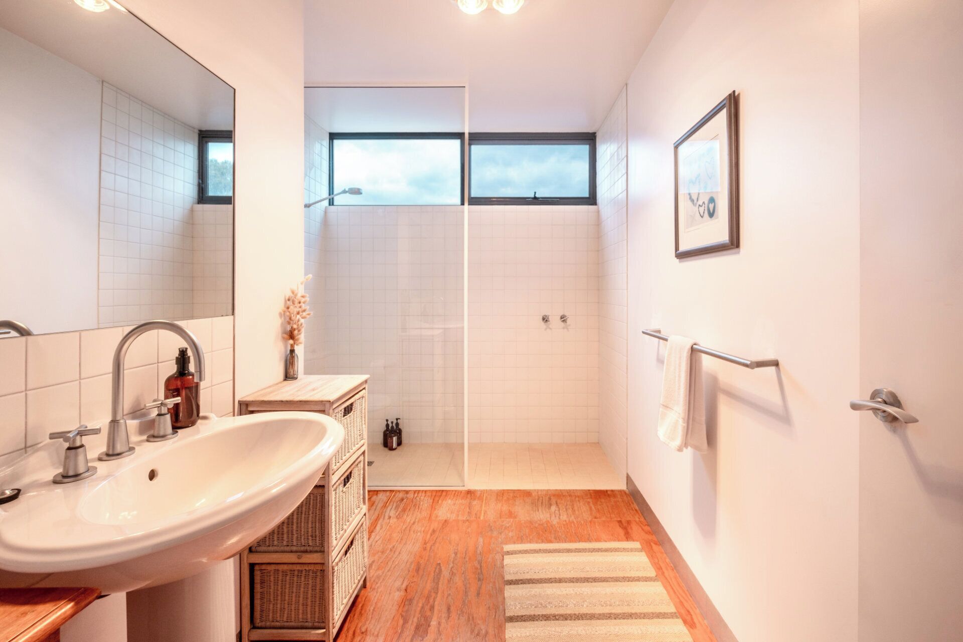 Une salle de bain moderne dotée d’un grand lavabo, d’un miroir, d’une douche et d’une fenêtre laissant entrer la lumière naturelle.
