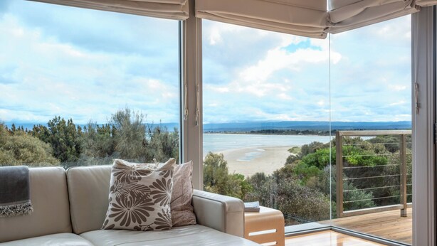 A modern living room with a sofa and a view of a beach and ocean. - Sea View - Freycinet Holiday Houses (Coles Bay)