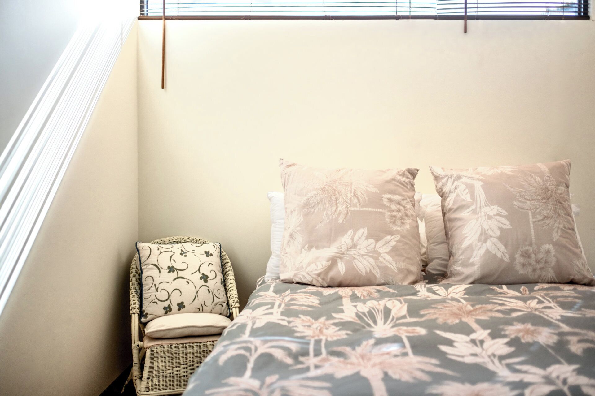 Ein Schlafzimmer mit einem Bett, zwei Kissen, einem Sessel und einem Fenster mit Jalousien.