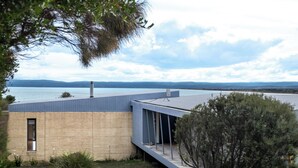 A modern building with a flat roof, large windows, and a view of a body of water and distant hills. - Sea View - Freycinet Holiday Houses (Coles Bay)