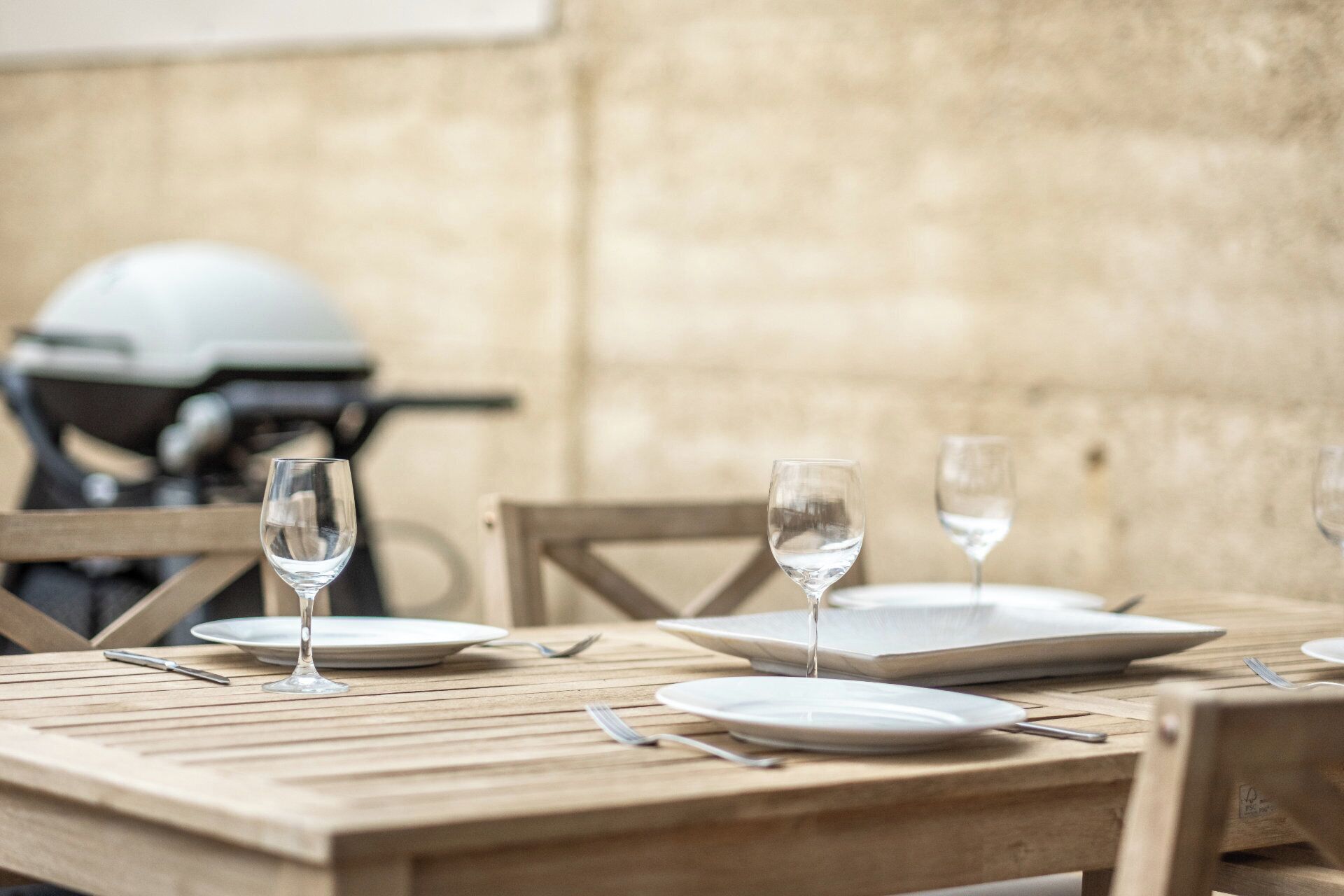 Una mesa de madera dispuesta con platos, cubiertos y dos copas de vino vacías.