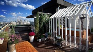 Une terrasse sur le toit dotée d’un espace salon extérieur moderne, d’une pergola et offrant une vue panoramique sur la ville.