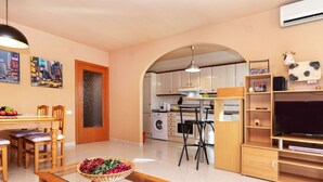 A modern kitchen with a dining area, a TV, and a living room with a TV and a basket of flowers. - Miami Dorada II by Interhome (Miami Platja)