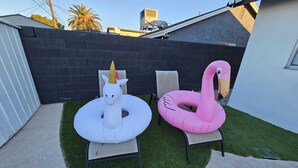 A backyard with artificial grass, two inflatable pool floats shaped like a unicorn and a flamingo, and a black brick wall. - Contemporary Modern Villa (Las Vegas)