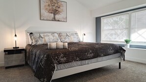 A bedroom with a bed, nightstands, a lamp, a window with blinds, and a wall-mounted painting. - Contemporary Modern Villa (Las Vegas)