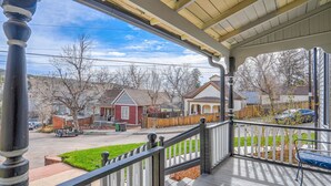 A covered porch with a wooden railing, a bench, and a view of a suburban street with houses and a clear sky. - Granite Grotto (Manitou Springs)