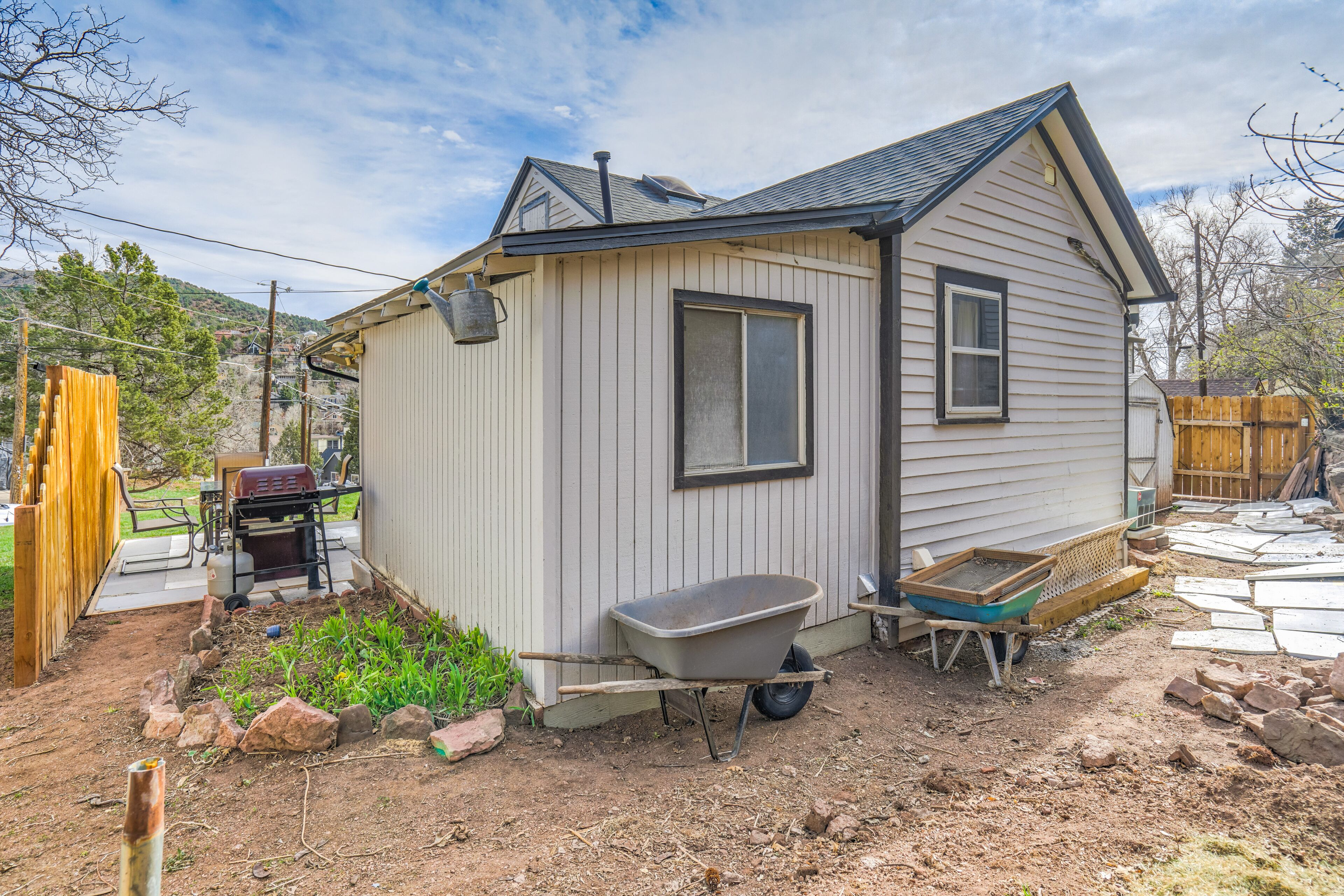 A small house with a single window, a wheelbarrow, and a wooden fence.