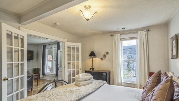 A bedroom with a large bed, a desk, a chair, a lamp, and a view of the outdoors. - Granite Grotto (Manitou Springs)