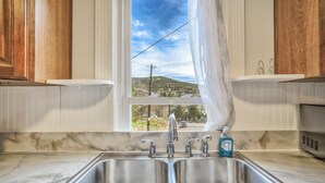 A kitchen with two stainless steel sinks, a window with a view of a hilly landscape, and wooden cabinets. - Granite Grotto (Manitou Springs)