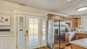 A kitchen with wooden cabinets, a stainless steel refrigerator, and a white door with frosted glass panels. - Granite Grotto (Manitou Springs)