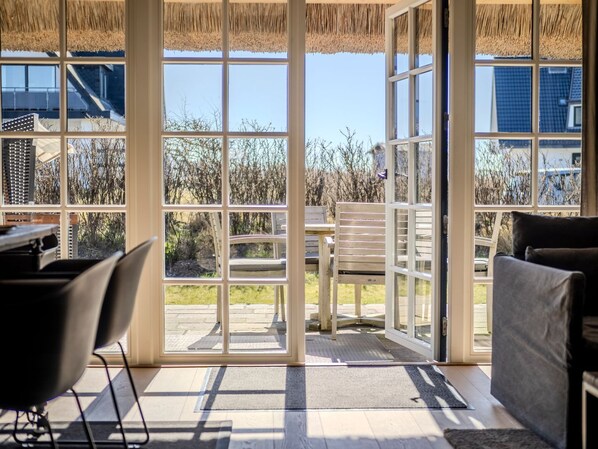 A sunlit room with large windows, a wooden table, and a chair.