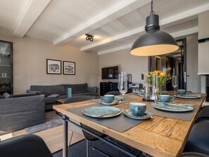 En moderne stue med et spiseområde. Der er en sofa, et sofabord og et spisebord dækket med blå tallerkener, glas og en vase med blomster.