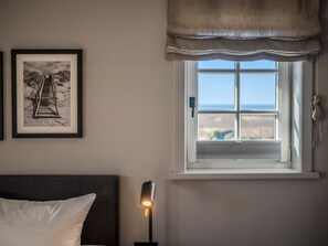 A bedroom with a bed, a bedside lamp, a framed picture on the wall, and a window with a view of the outdoors.