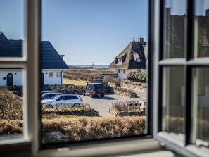 Un village côtier avec des maisons traditionnelles aux toits de chaume, une voiture garée et une vue dégagée sur la mer.