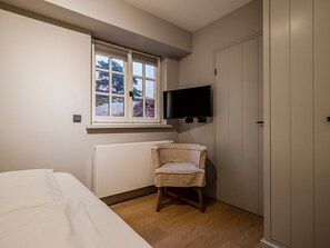 Ein Schlafzimmer mit Bett, Stuhl, Wandfernseher, Fenster und Kleiderschrank.