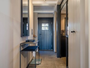 Un couloir avec une porte sombre, une petite table sur laquelle se trouve un appareil, et un miroir accroché au mur.